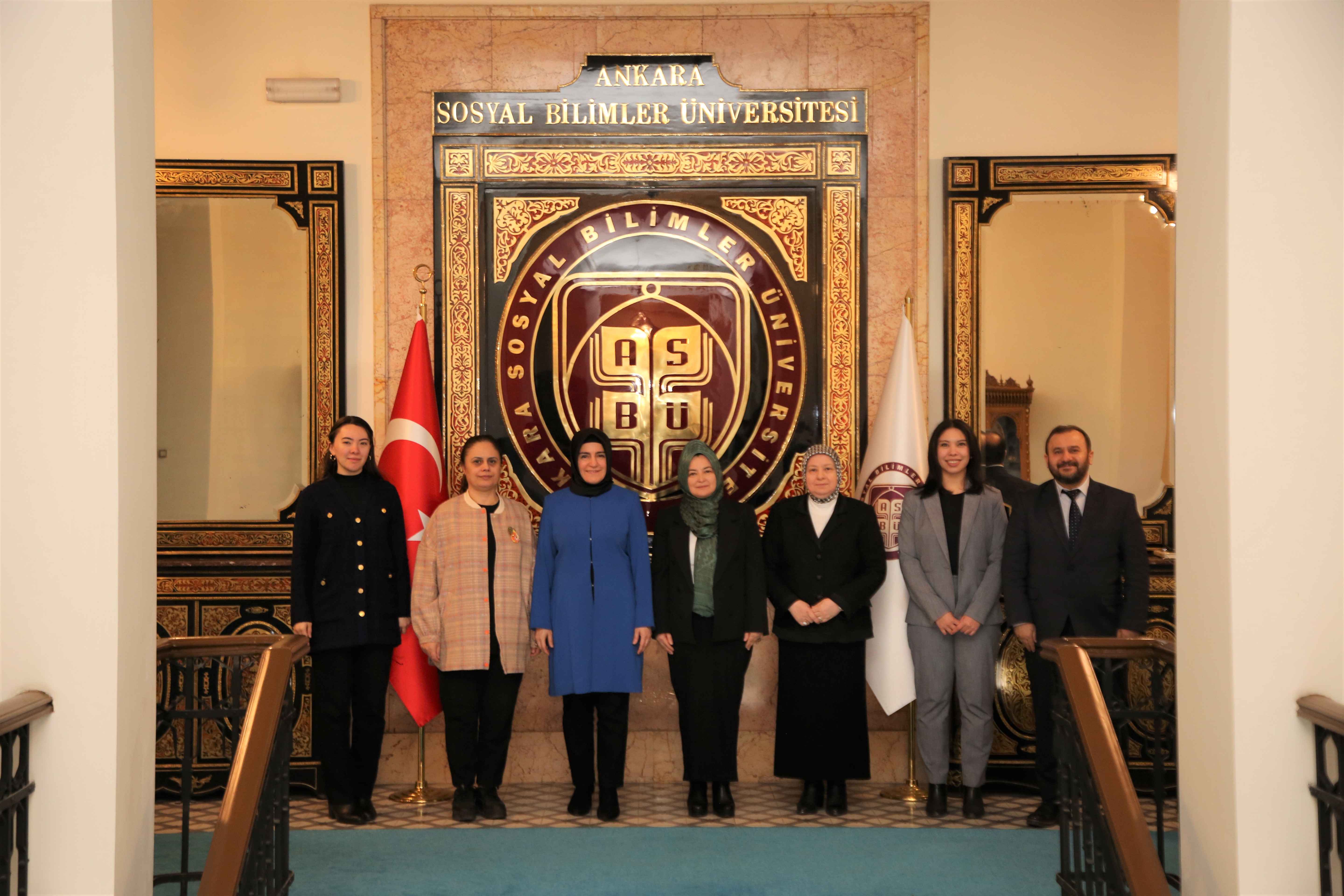 Prof. Dr. Münire Kevser Baş ve Konuklar rektörlük binasında Asbü logosu önünde fotoğraf çektiriyorlar