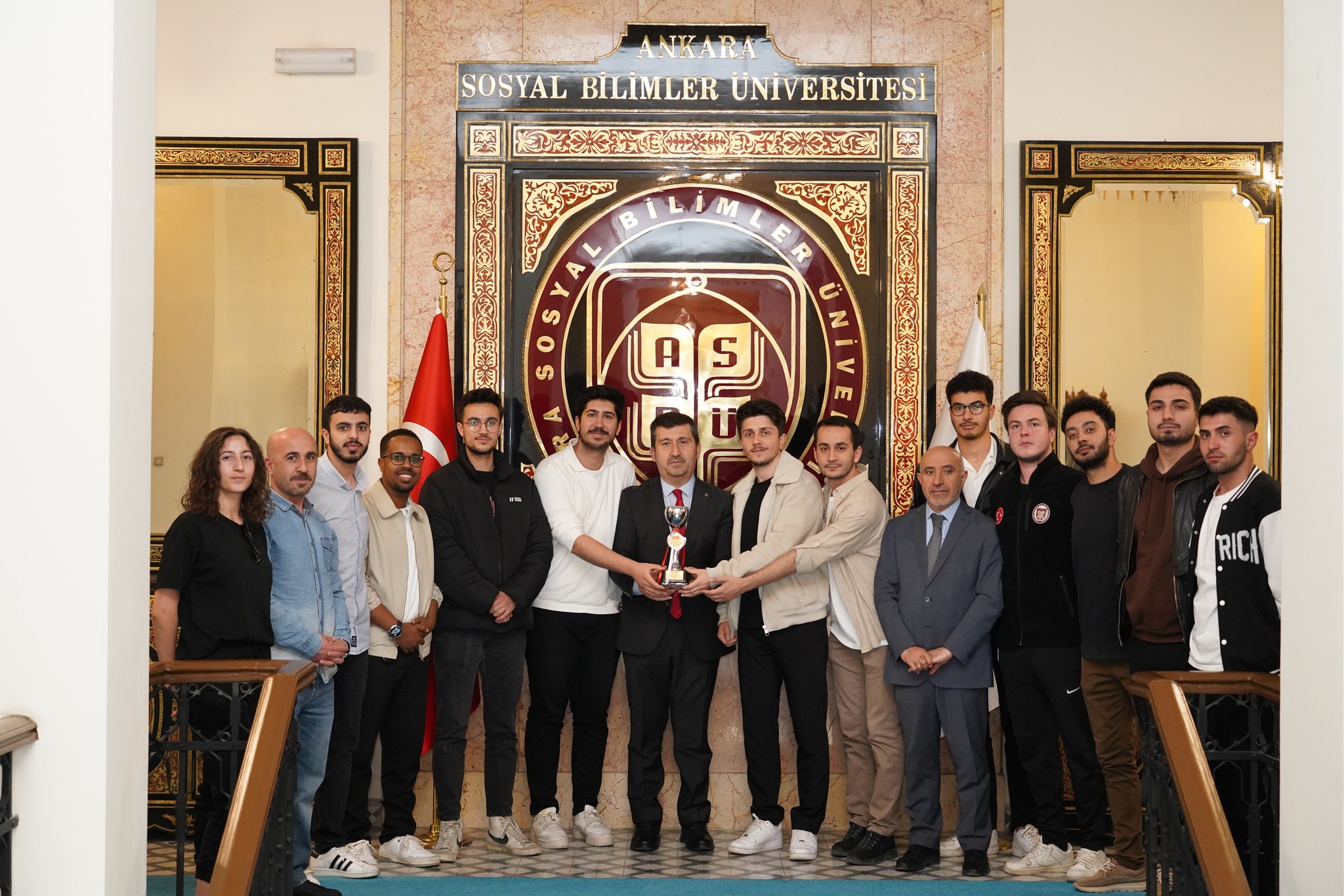 Prof. Dr. Musa Kazım Arıcan ASBÜ futsal takımı ile ASBÜ Rektörlük Binasında ASBÜ Logosu önünde fotoğraf çektiriyor.