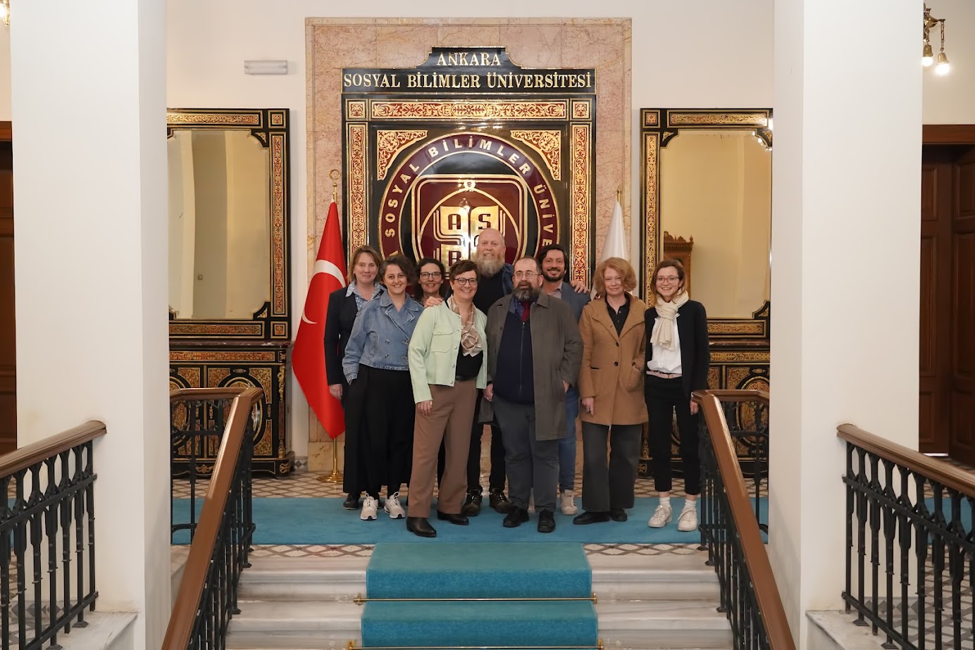 Doç. Dr. Aysel SARICAOĞLU AYGAN ve Konuklar Rektörlük binası ASBÜ logosu  önünde fotoğraf çektiriyorlar.